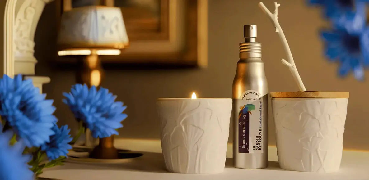 Sandalwood Sacré candle, pillow mist, and diffuser from the Wellbeing Collection by Le Jardin Retrouvé, displayed on a living room table with blue flowers on the side