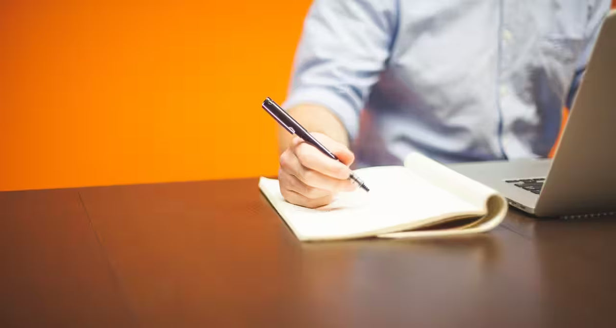 A man writing in front of a laptop, in a meeting